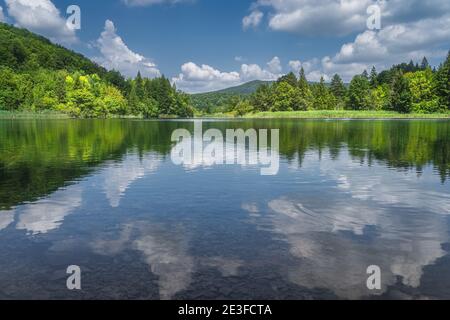 Nuvole riflesse in lago pulito circondato da colline e verde lussureggiante foresta, Plitvice Lakes National Park patrimonio mondiale dell'UNESCO in Croazia Foto Stock