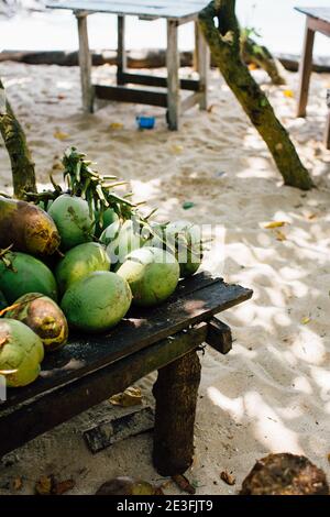 Colpo verticale di alcune noci di cocco fresche su un tavolo di legno in spiaggia Foto Stock