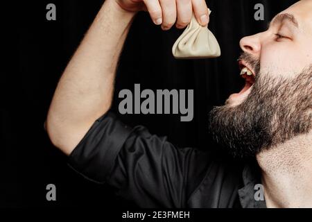 L'uomo bearded sta mangiando emotivamente khinkali. Il khinkali piatto georgiano nazionale. Concetto di pubblicità foto di khinkali Foto Stock