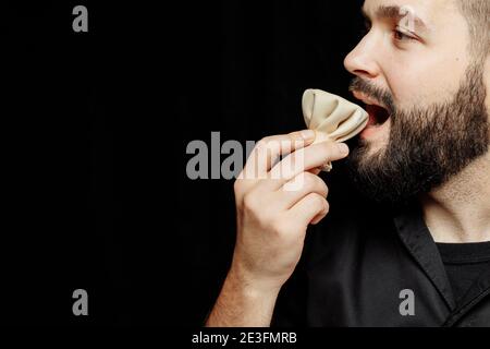 L'uomo bearded sta mangiando emotivamente khinkali. Il khinkali piatto georgiano nazionale. Concetto di pubblicità foto di khinkali Foto Stock