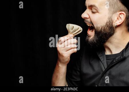 L'uomo bearded sta mangiando emotivamente khinkali. Il khinkali piatto georgiano nazionale. Concetto di pubblicità foto di khinkali Foto Stock