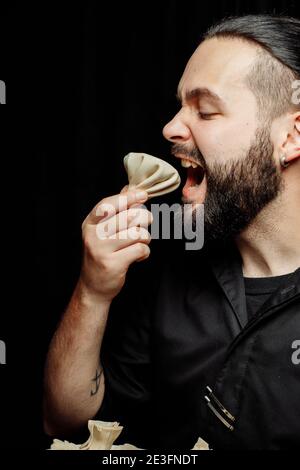 L'uomo bearded sta mangiando emotivamente khinkali. Il khinkali piatto georgiano nazionale. Concetto di pubblicità foto di khinkali Foto Stock