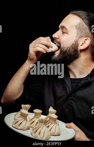 L'uomo bearded sta mangiando emotivamente khinkali. Il khinkali piatto georgiano nazionale. Concetto di pubblicità foto di khinkali Foto Stock