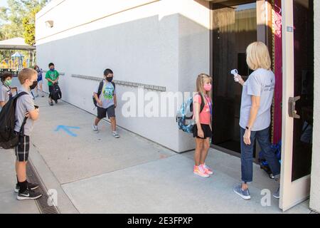 Usando un termometro digitale, un insegnante della scuola elementare della California controlla le temperature dei suoi allievi che arrivano multirazziali mentre arrivano per il dur della classe Foto Stock