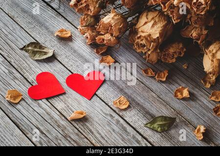 Due cuori rossi con petali di rose secche su legno tabella Foto Stock