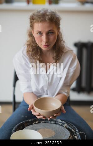 Il lavoro è terminato. Giovane ceramista femminile al chiuso con prodotto finito di argilla fatta a mano. Concezione della ceramica Foto Stock