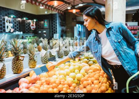 Giovane donna in giacca denim acquista frutta in negozio Foto Stock