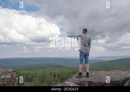 Un uomo di mezza età si trova sulla cima della montagna e mostra la strada da dove andare. Concetto di viaggio e vita attiva. Raggiungimento dell'obiettivo. Spazio di copia Foto Stock