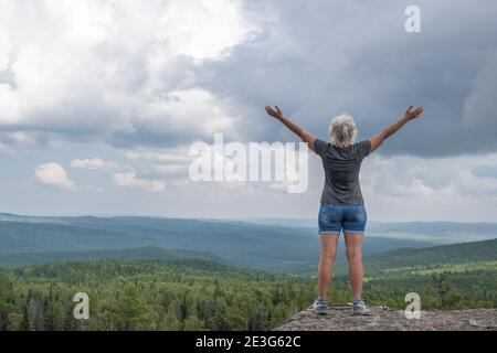 Felice donna di mezza età alzando le mani si trova sulla cima della montagna, ammirando la bella view.Freedom, gioia e obiettivo Achievement.Copy spazio. Foto Stock