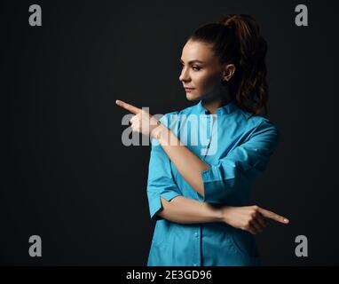 Giovane donna bruna infermiera medico in punti blu abito medico con le dita in direzioni diverse diagonali Foto Stock