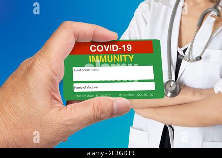 Mano che tiene covid-19 certificato immune con medico femminile su sfondo blu. Foto Stock