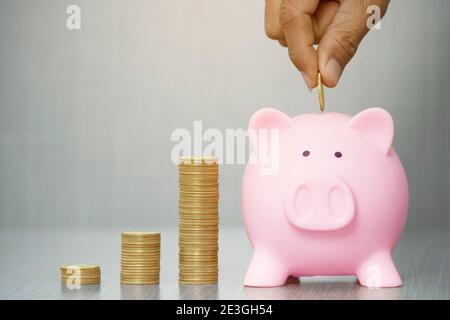 Mano mettendo moneta d'oro a banca piggy su sfondo grigio. Con copia space.Saving investimento concetto Foto Stock