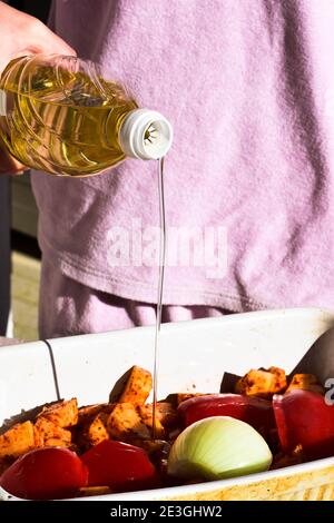 Lo chef versa l'olio da cucina dalla bottiglia su patate grezze/cibo preparazione/ Foto Stock