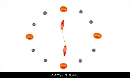 Un orologio di pomodori ciliegini, mirtilli e peperoncini rossi su sfondo bianco che mostra l'ora. Spazio per il testo. Foto Stock