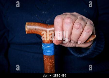 Le mani di una donna anziana su un vecchio bastone da passeggio con manici a forma di t. Il concetto di vecchiaia, solitudine, sollecitudine e cura degli anziani. Foto Stock