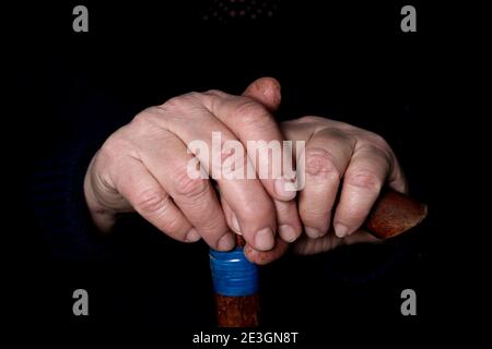 Le mani di una donna anziana su un vecchio bastone da passeggio con manici a forma di t. Il concetto di vecchiaia, solitudine, sollecitudine e cura degli anziani. Foto Stock