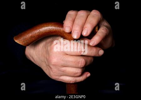 Le mani di una donna anziana su un vecchio bastone da passeggio con manici a forma di t. Il concetto di vecchiaia, solitudine, sollecitudine e cura degli anziani. Foto Stock