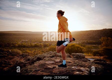 Atleta maschile facendo esercizio di allungamento delle gambe preparazione per il run in sentiero natura al mattino con vista dell'alba Foto Stock