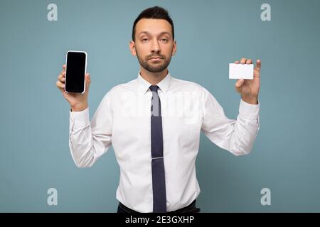 Foto di un bel brunetto con barba che indossa casual camicia bianca e cravatta isolato su sfondo blu con spazio vuoto che tiene in mano Foto Stock