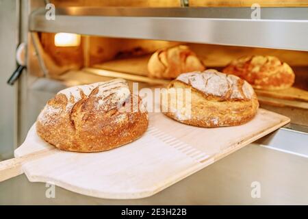 Baker mettendo il pane nel forno del pane accovacciata sul pavimento del forno Foto Stock