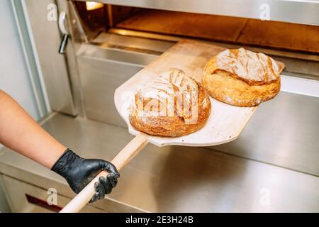 Baker mettendo il pane nel forno del pane accovacciata sul pavimento del forno Foto Stock