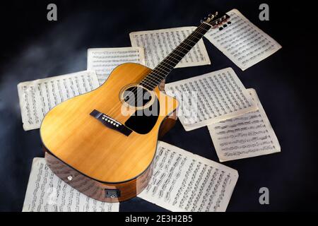 set di spartiti musicali e classico acustico a sei corde di colore giallo chitarra con pickguard nero su sfondo nero isolato Foto Stock