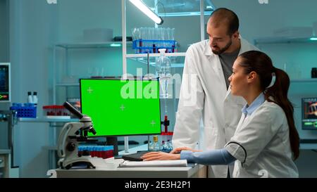 Moderno laboratorio di ricerca medica con due scienziati che utilizzano un computer con schermo a tasti cromatici verde. Medici specialisti discutere di trattamento innovativo, laboratorio scientifico avanzato per la medicina. Foto Stock