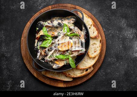 Cozze cotte in padella con formaggio e foglie di basilico, su tavola di legno, su fondo scuro Foto Stock