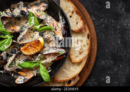 Cozze cotte in padella con formaggio e foglie di basilico, su tavola di legno, su fondo scuro Foto Stock