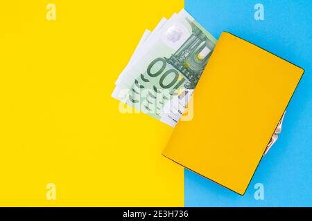 Primo piano del portafoglio giallo con banconote da 100 euro su sfondo colorato. Foto Stock