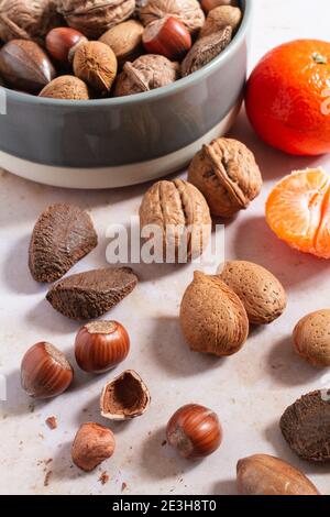 Assortimento di dadi misti in una ciotola con alcuni dadi spaccati sul lato e una clementina fresca. Foto Stock