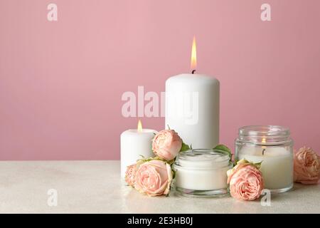 Candele e rose profumate su tavola bianca su sfondo rosa Foto Stock