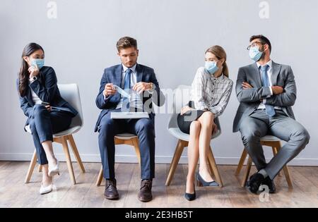 Multiculturale persone di affari in maschere mediche guardando l'uomo con computer portatile nella hall Foto Stock