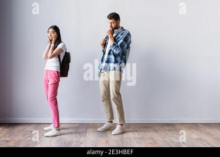 Preoccupato studente asiatico in piedi vicino all'uomo in sala prima dell'esame Foto Stock