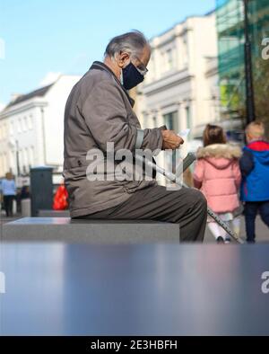 Un uomo si siede su una panchina per leggere una lista della spesa in High Street, Cheltenham durante la pandemia di Coronavirus in corso. Foto Stock