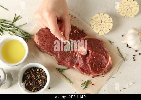 La mano femminile mette il rosmarino sulla carne di bistecca cruda, primo piano Foto Stock