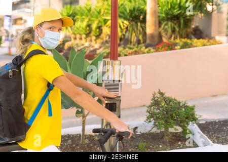 Giovane donna con borsa termica o zaino in bicicletta lungo la città, che consegna il cibo. Corriere, servizio di consegna e concetto di coronavirus. Mai Foto Stock