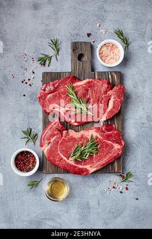 Due bistecche fresche di manzo prime Black Angus a base di carne cruda, Rib Eye, Denver, su tagliere di legno. Vista dall'alto, posiziona per il testo. Foto Stock