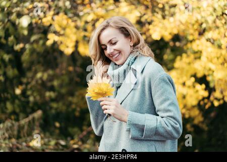 Affascinante giovane donna allegra in un paesaggio di parco autunnale con un bouquet di foglie gialle. Foto Stock