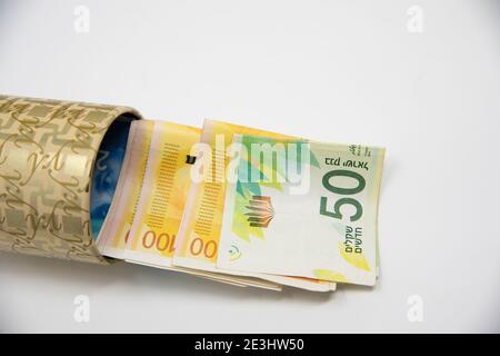 Banca di porcellini di metallo con i simboli di New Israel Shekel per risparmiare denaro. Su sfondo bianco con banconote NIS. Salvataggio di fogli in una scatola di latta. Tenere le banconote in un conto di risparmio improvvisato. Concept Foto di alta qualità Foto Stock
