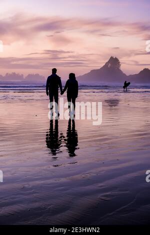 Coppia di uomini e donne di mezza età guardando il tramonto sulla spiaggia di Tofino Vancouver Island Canada, bellissimo tramonto sulla spiaggia con colori rosa-viola nel cielo. Canada Tofino Foto Stock