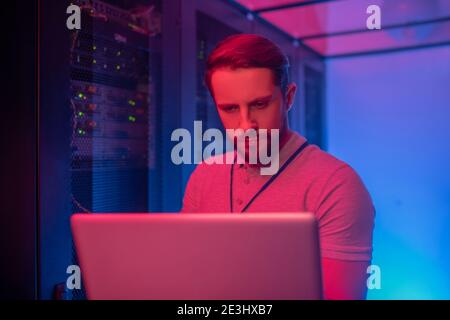 Uomo concentrato con notebook in piedi vicino al server Foto Stock