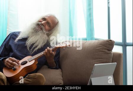 UN VECCHIO UOMO SOPPORTATO CHE SI SIEDE FELICEMENTE E GIOCA LO STRUMENTO DI UKULELE Foto Stock