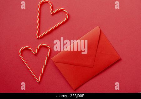 Festivo sfondo rosso. Cuori di dolci caramelle con busta. Amore. San Valentino. 14 di febbraio. Disposizione piatta, vista dall'alto. Foto Stock