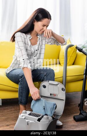 giovane donna allergica che strofina il naso tenendo la polvere dell'aspirapolvere borsa Foto Stock