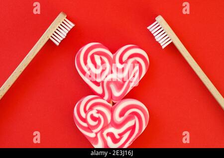 Festivo sfondo rosso. Dolce caramella a forma di cuore. E due spazzolini da denti come un simbolo di amore. San Valentino. 14 di febbraio. Idee di regali. Piatto la Foto Stock