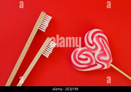 Festivo sfondo rosso. Dolce caramella a forma di cuore. E due spazzolini da denti come un simbolo di amore. San Valentino. 14 di febbraio. Idee di regali. Piatto la Foto Stock