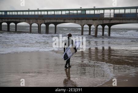 Un surfista si fa strada nel mare al largo della spiaggia di Boscombe a Dorset. Data immagine: Martedì 19 gennaio 2021. Foto Stock