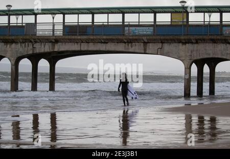 Un surfista si fa strada nel mare al largo della spiaggia di Boscombe a Dorset. Data immagine: Martedì 19 gennaio 2021. Foto Stock