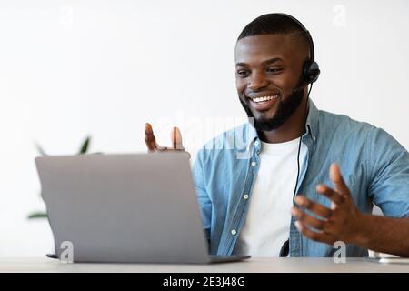 Videoconferenza. Allegro afroamericano uomo in cuffia facendo web call sul portatile Foto Stock